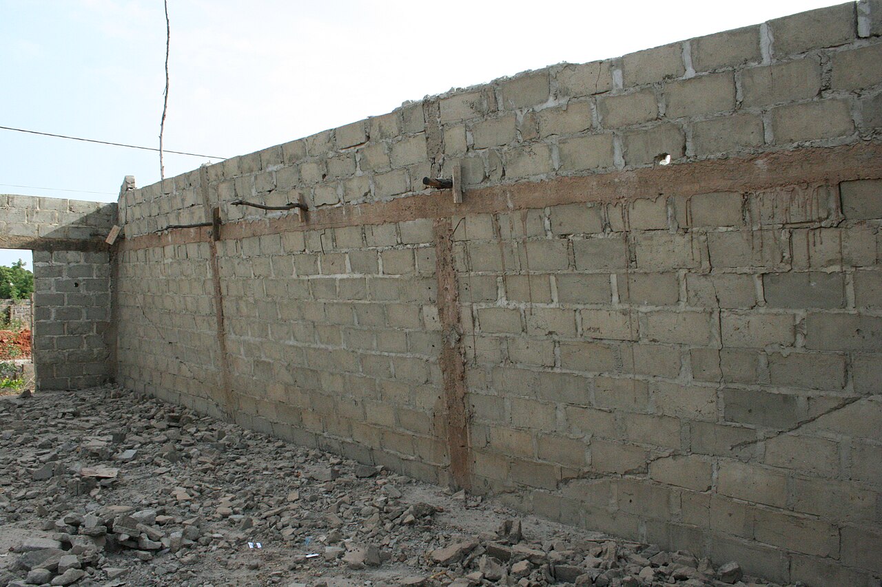 An unfinished concrete block wall with a long crack, standing on rubble.