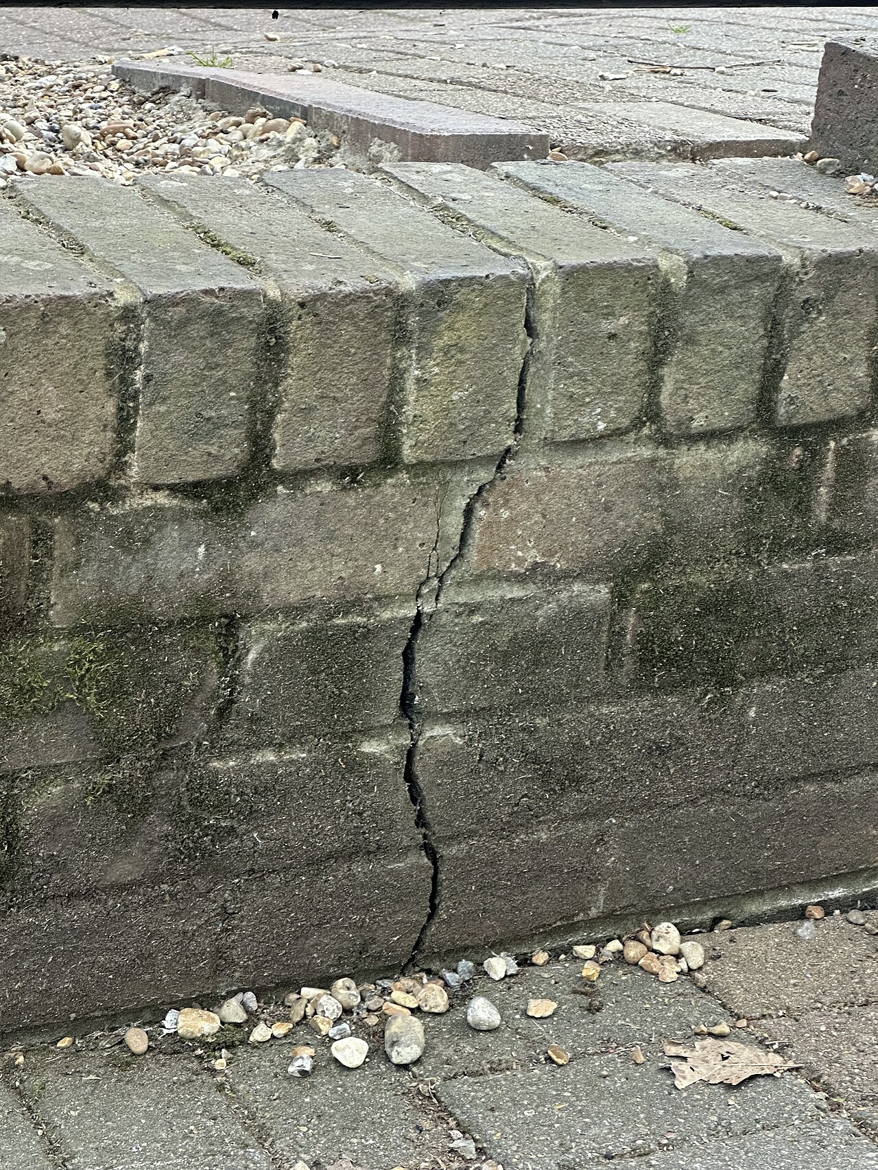 A crack running down a low brick retaining wall beside a paved path.