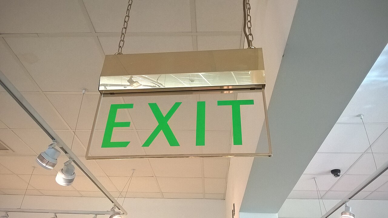 An illuminated green EXIT sign hanging on chains from a tiled ceiling.