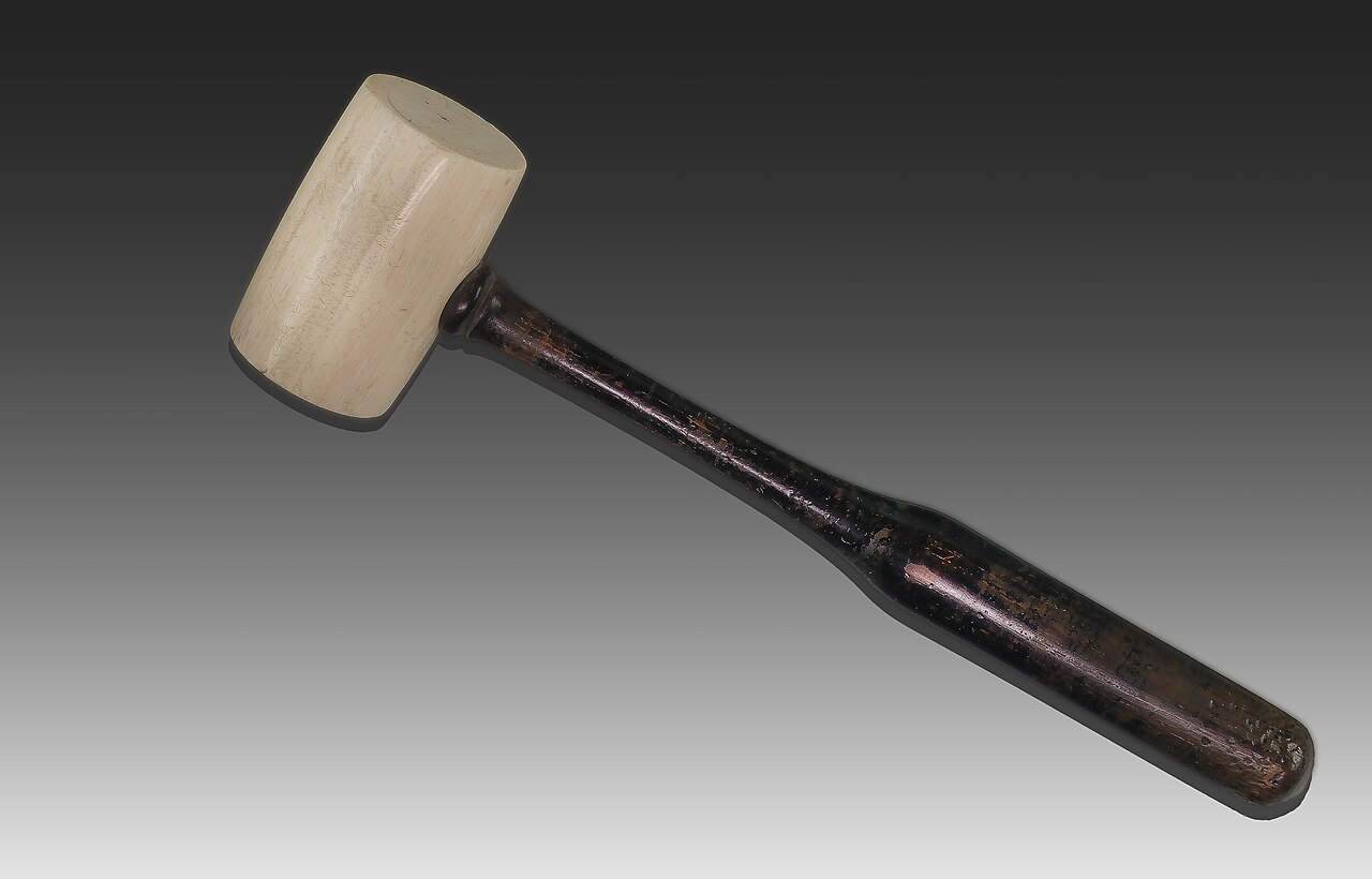 A wooden mallet with a pale head and a dark handle on a grey background.