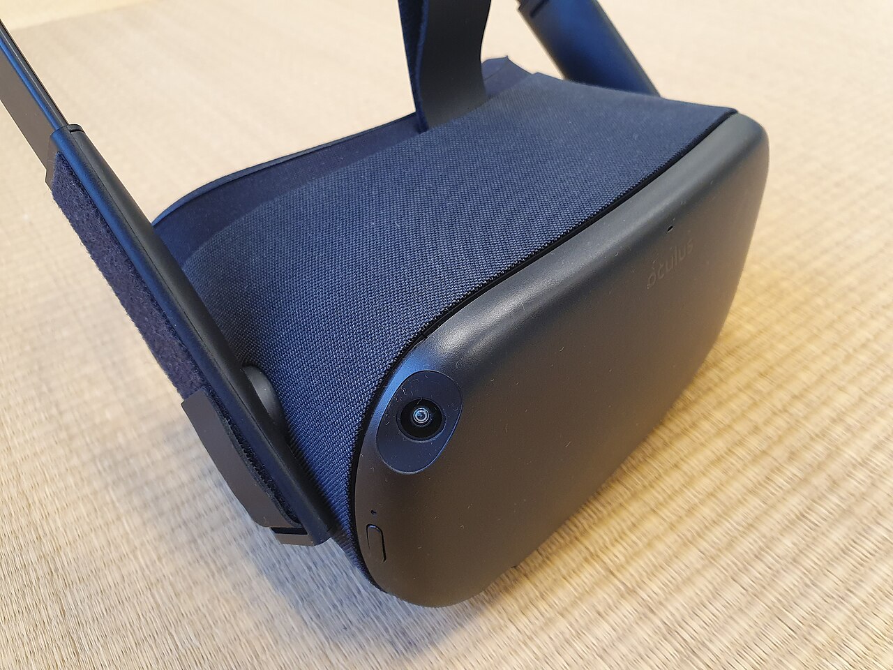 A standalone VR headset with a fabric-covered front, lying on a woven mat.