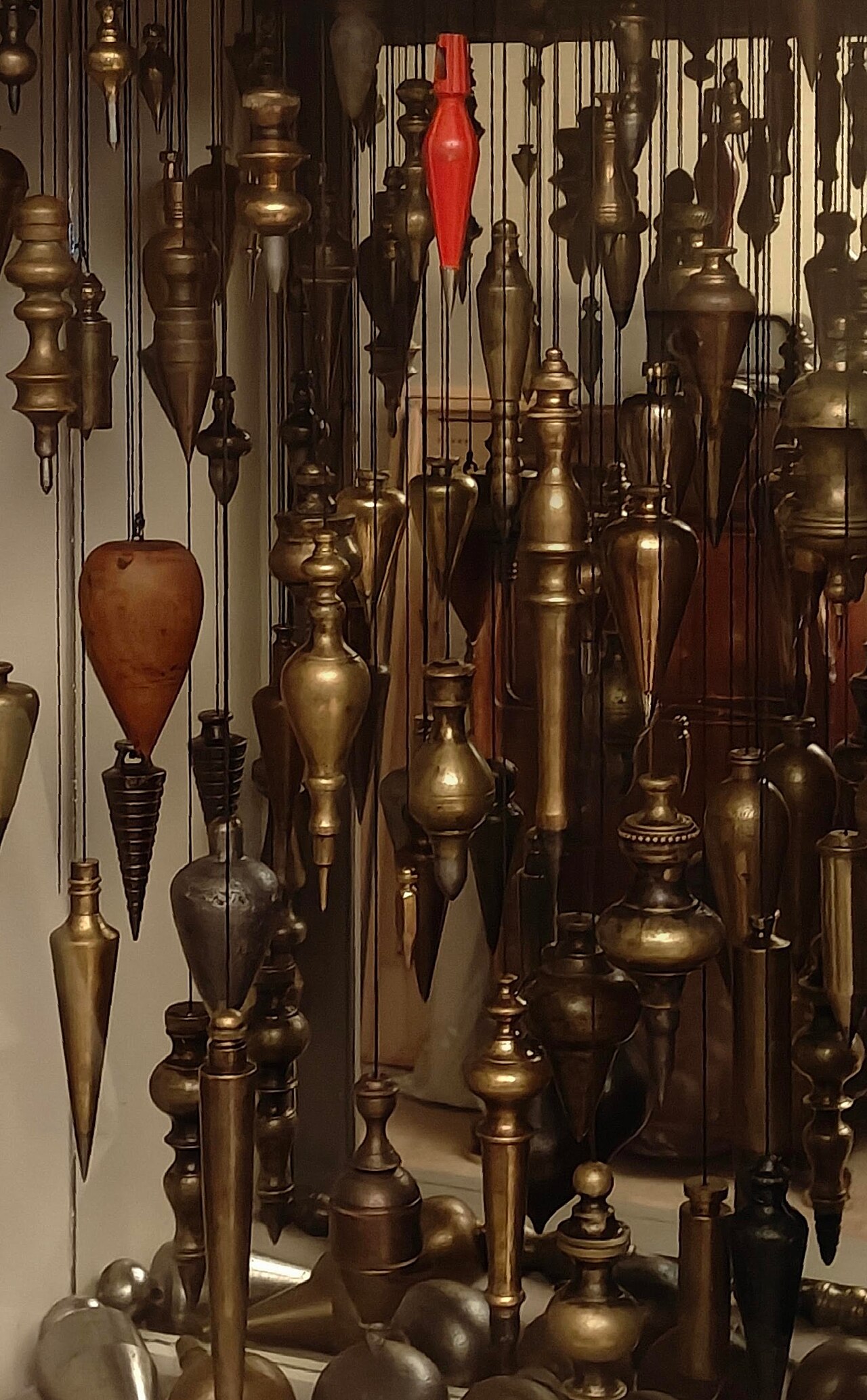 Dozens of brass, iron and wooden plumb bobs hanging on strings at different heights.