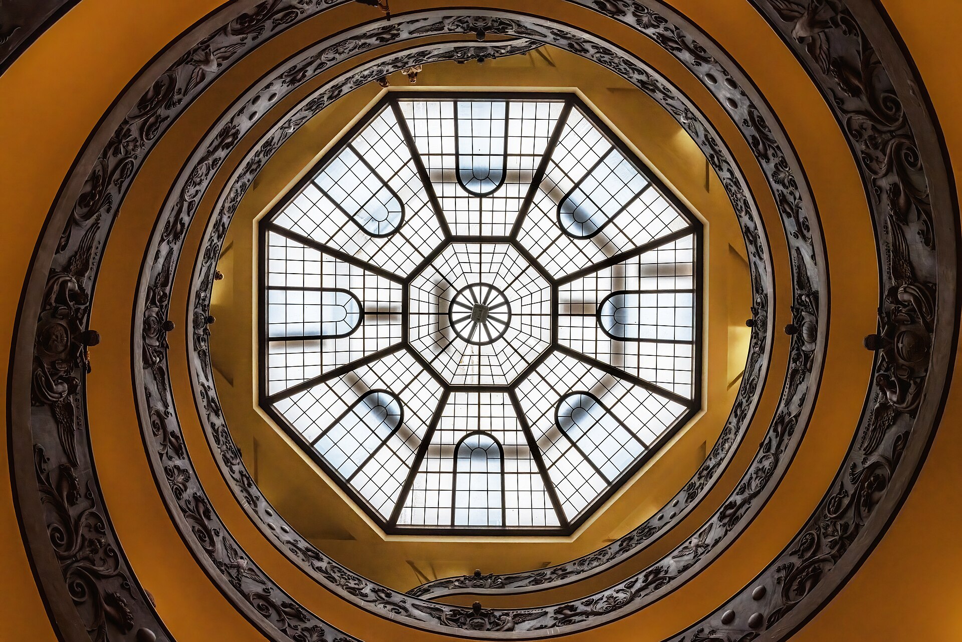 Looking up through a golden spiral staircase to an octagonal glass skylight.