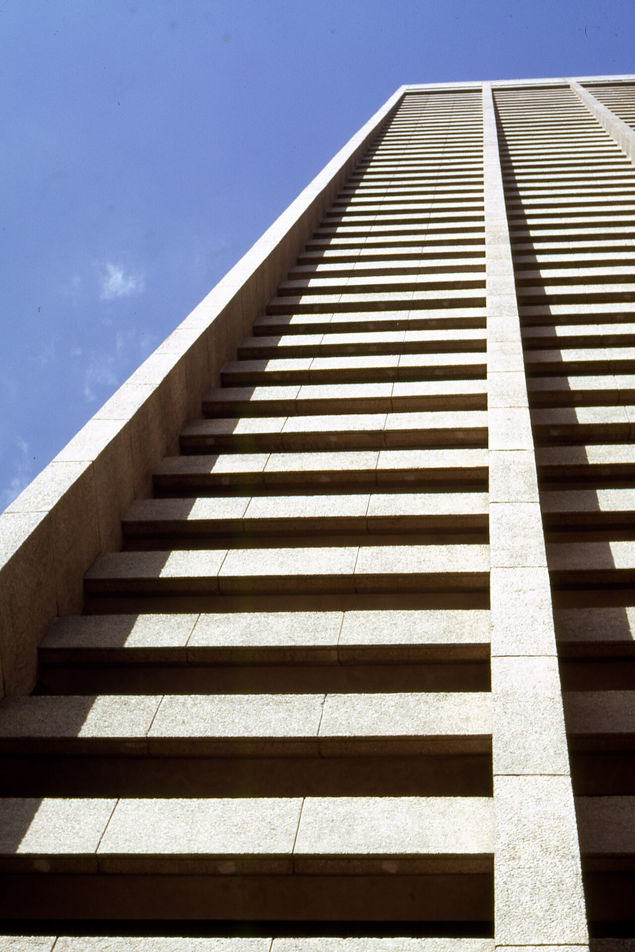 Looking straight up the stone facade of a tall office tower against a blue sky.